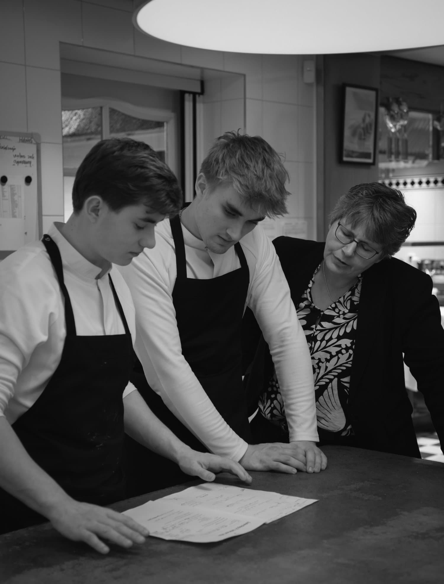 Two young cooks being talked through the work at the kitchen counter